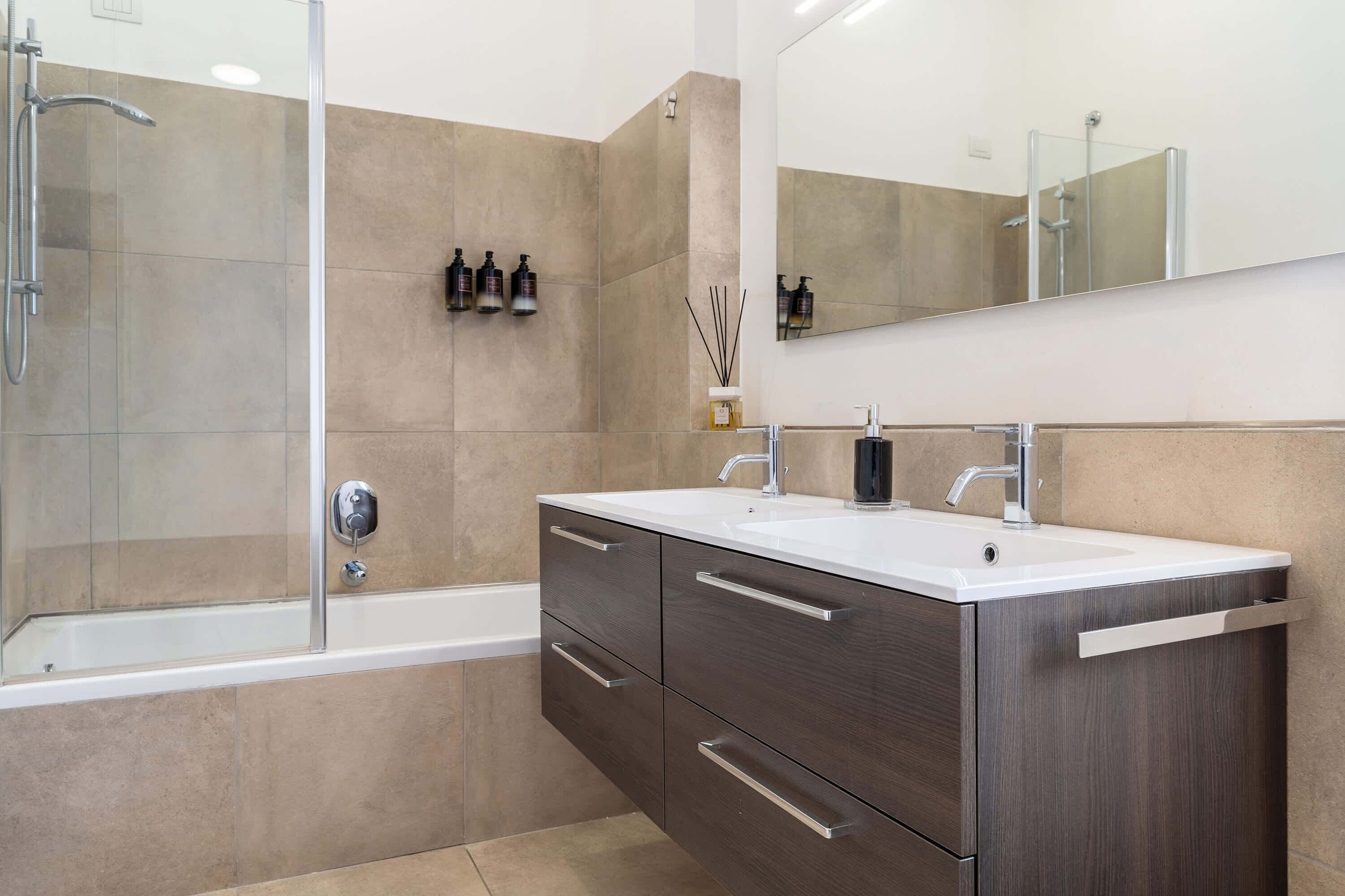 Ein modernes Badezimmer mit Badewanne, zwei Waschbecken, einem großen Spiegel und einer Duschkabine.