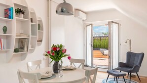 Un coin repas avec une table ronde, des chaises blanches, un vase avec des fleurs et un fauteuil doté d’un repose-pieds.