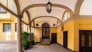 Un couloir couvert avec un escalier, des colonnes et une lampe.