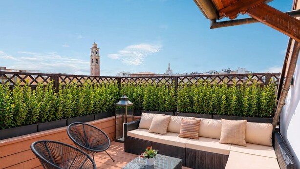 Une terrasse sur le toit, aménagée avec un canapé, des chaises, une table et offrant une vue sur une tour.