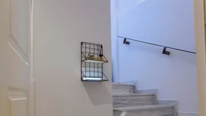 A staircase with a white wall, a metal shelf with items, and a door. - Green Hill Recreational Luxury (Iraklio)