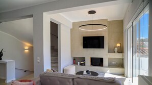A modern living room with a sofa, a fireplace, and a TV mounted on the wall. - Green Hill Recreational Luxury (Iraklio)