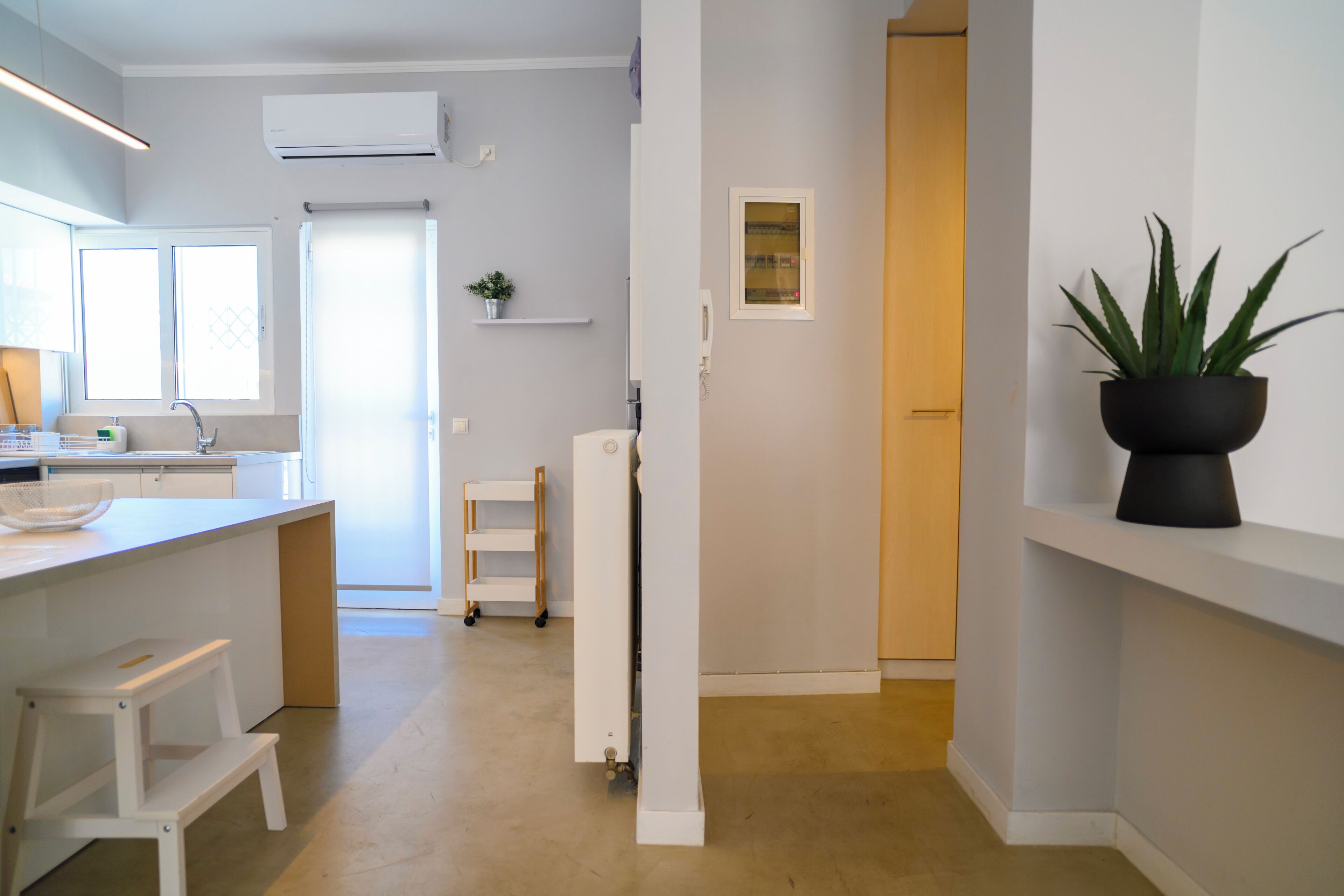 A modern kitchen with a white countertop, a white stool, and a potted plant.