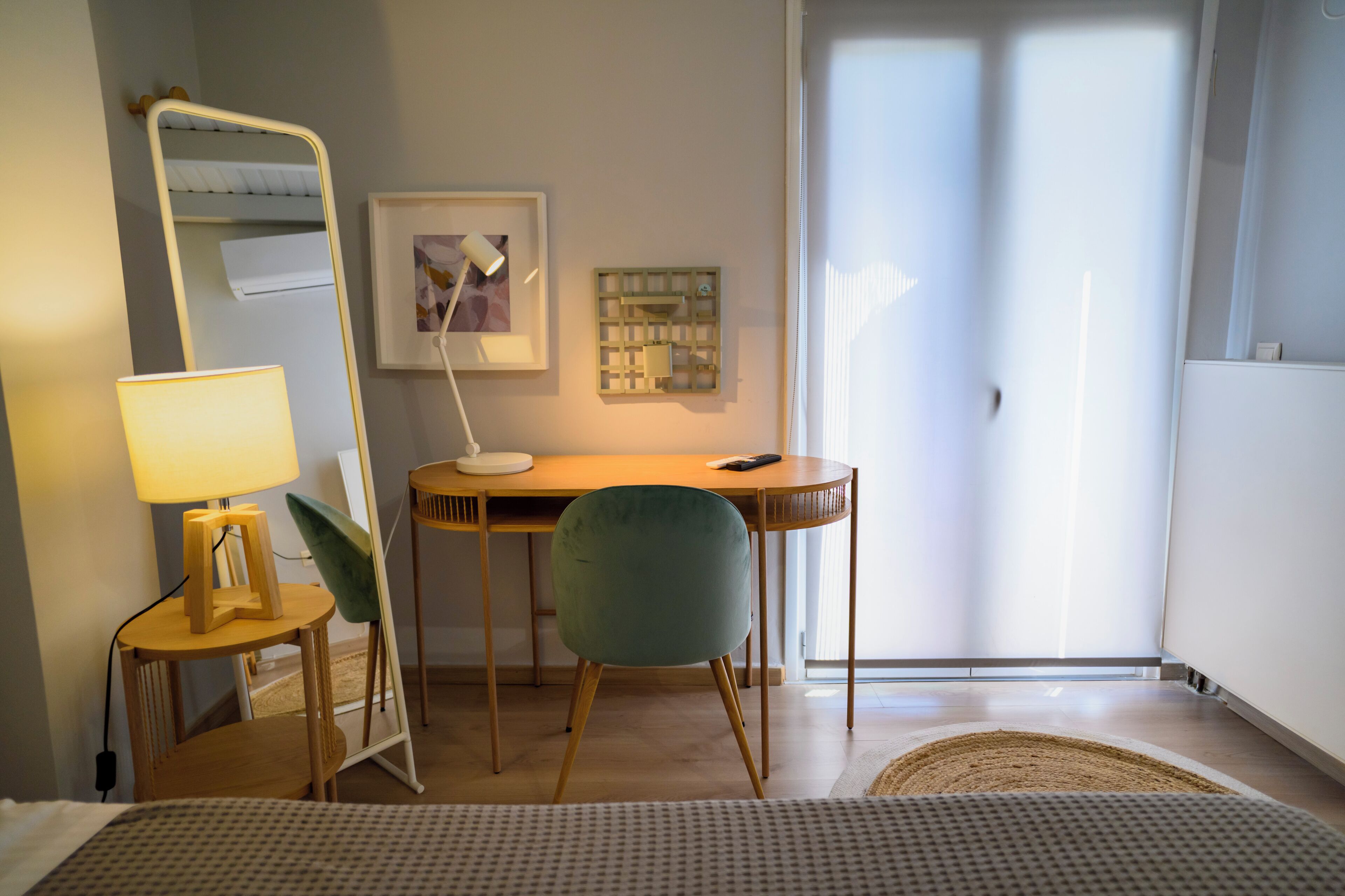 Una habitación con cama, escritorio con silla, lámpara, cuadro enmarcado y ventana.