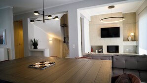 Una sala moderna con una mesa de comedor de madera, un sofá, un televisor montado en la pared y una escalera que conduce a otro nivel.