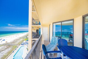 A balcony with a view of the beach, a pool, and a dining area with chairs and tables. - Phoenix V 916 2 Bedroom Condo (Orange Beach)