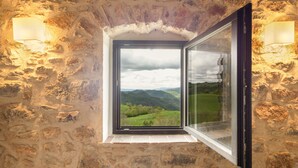Un mur de pierre avec une fenêtre, une lampe et une vue sur des collines verdoyantes.