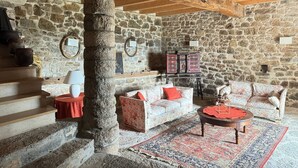 Une pièce rustique aux murs de pierre, avec un escalier en bois, un canapé, une table basse et un tapis à motifs.