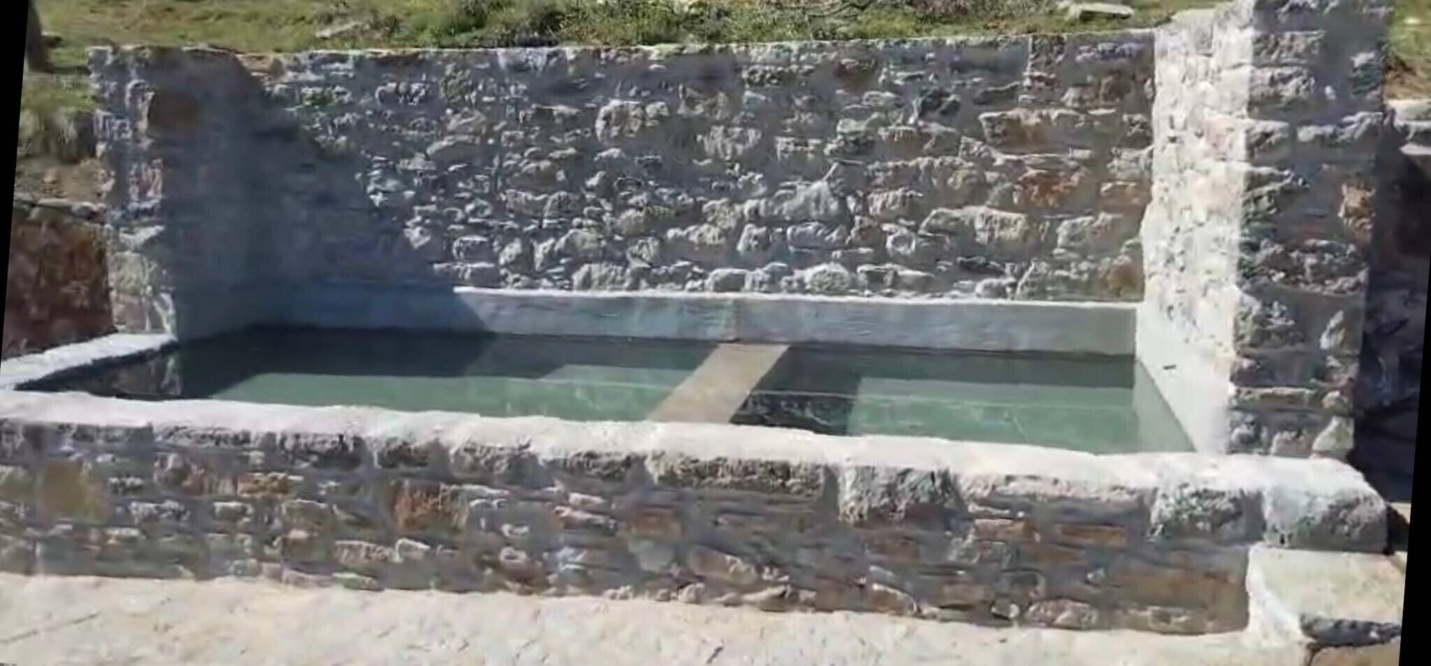 Una edificación de piedra con una piscina rectangular.