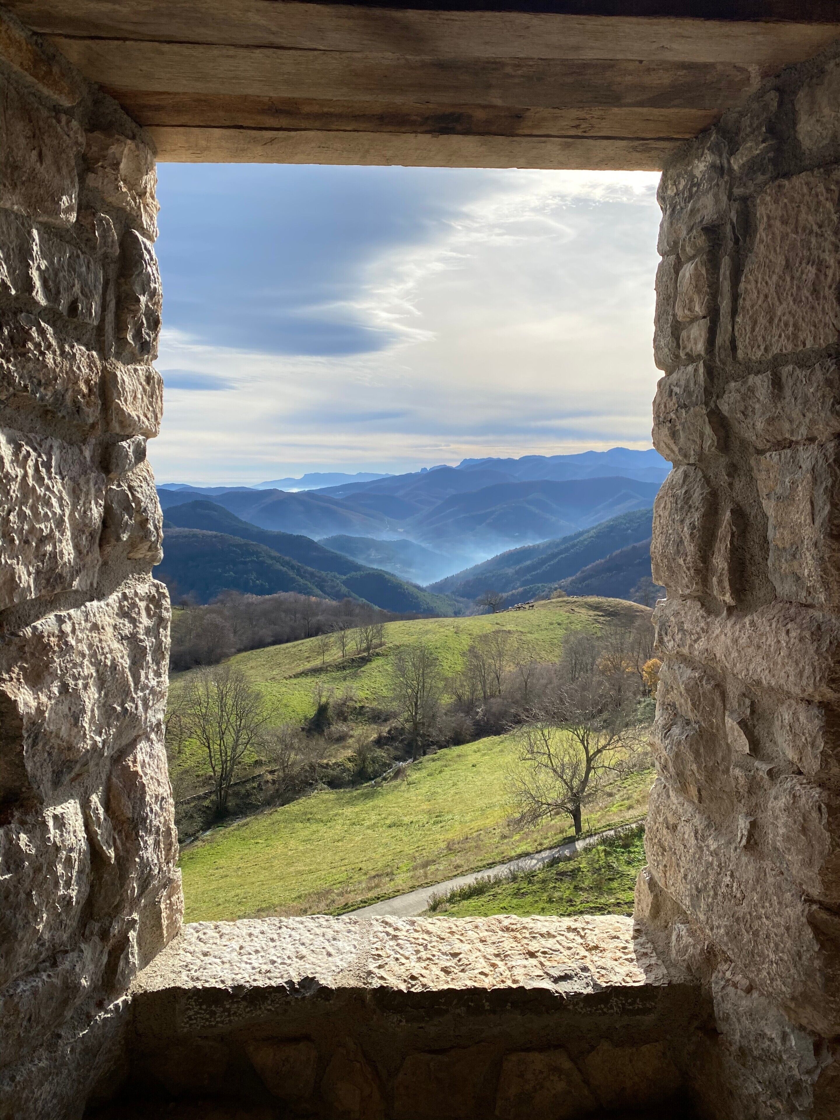 A stone window with a view of rolling hills and distant mountains.