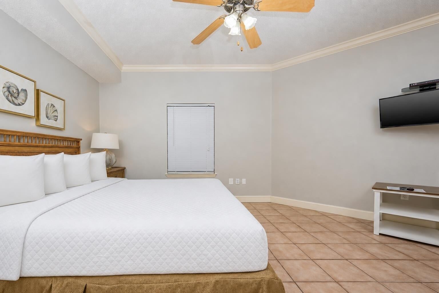 Una habitación de hotel con cama, ventilador de techo, televisión y ventana con persianas.