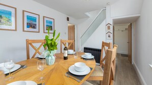 Un coin repas avec une table ronde, des chaises, une bouteille de vin et des tableaux encadrés accrochés au mur.