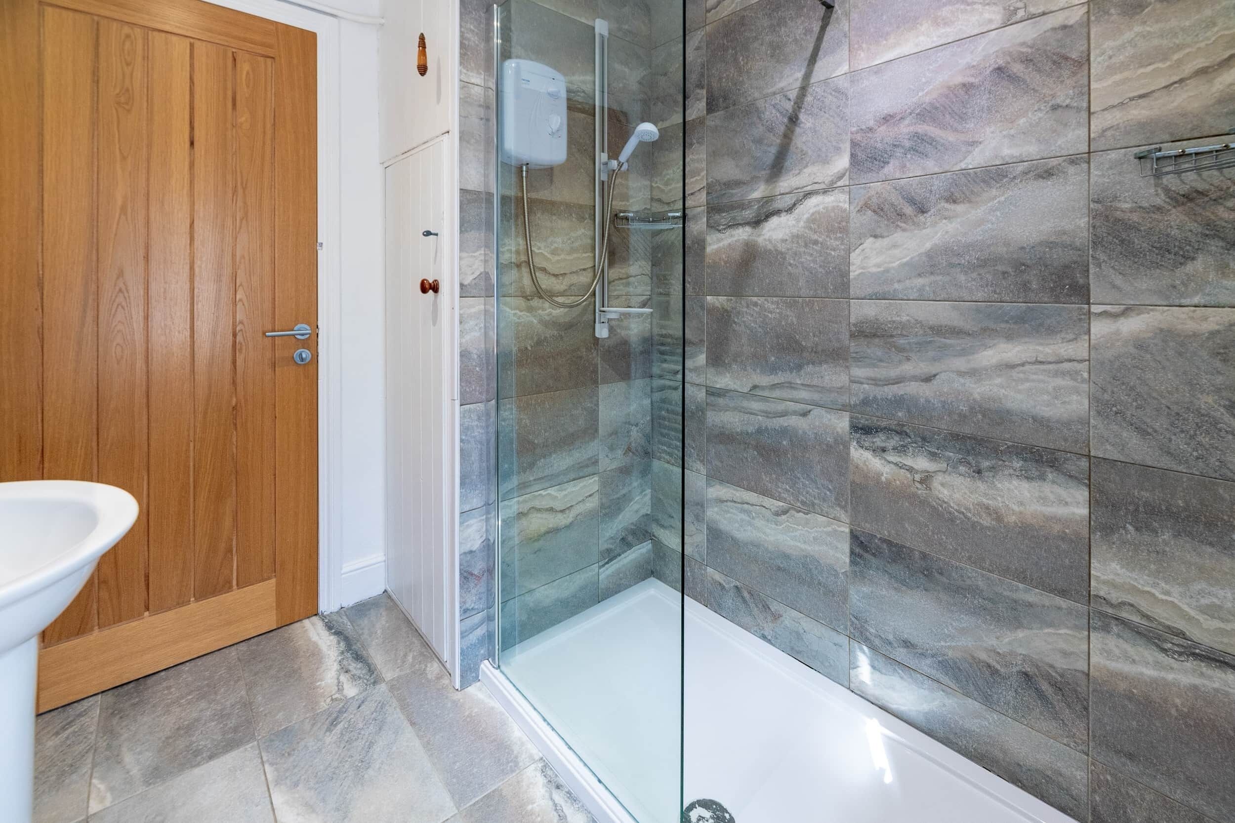 Un baño con ducha acristalada, puerta de madera y lavabo blanco.