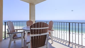 A balcony with a view of the beach, a table, and two Adirondack chairs. - Phoenix V 1215 2 Bedroom Condo (Orange Beach)