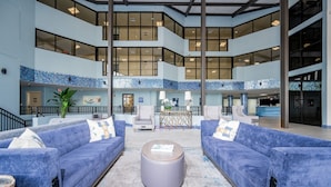 A spacious lobby with a high ceiling, blue-tiled walls, and a central seating area with two sofas and a round coffee table. - Phoenix V 1215 2 Bedroom Condo (Orange Beach)