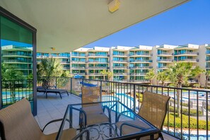 A balcony with chairs, a pool, and a view of a multi-story building with balconies. - Phoenix On The Bay 1212 2 Bedroom Condo (Orange Beach)