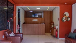 Un área de recepción con un escritorio de madera, sofás de cuero, un extintor y un elemento decorativo en la pared.