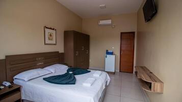 A hotel room with a bed, wardrobe, TV, and a small refrigerator.