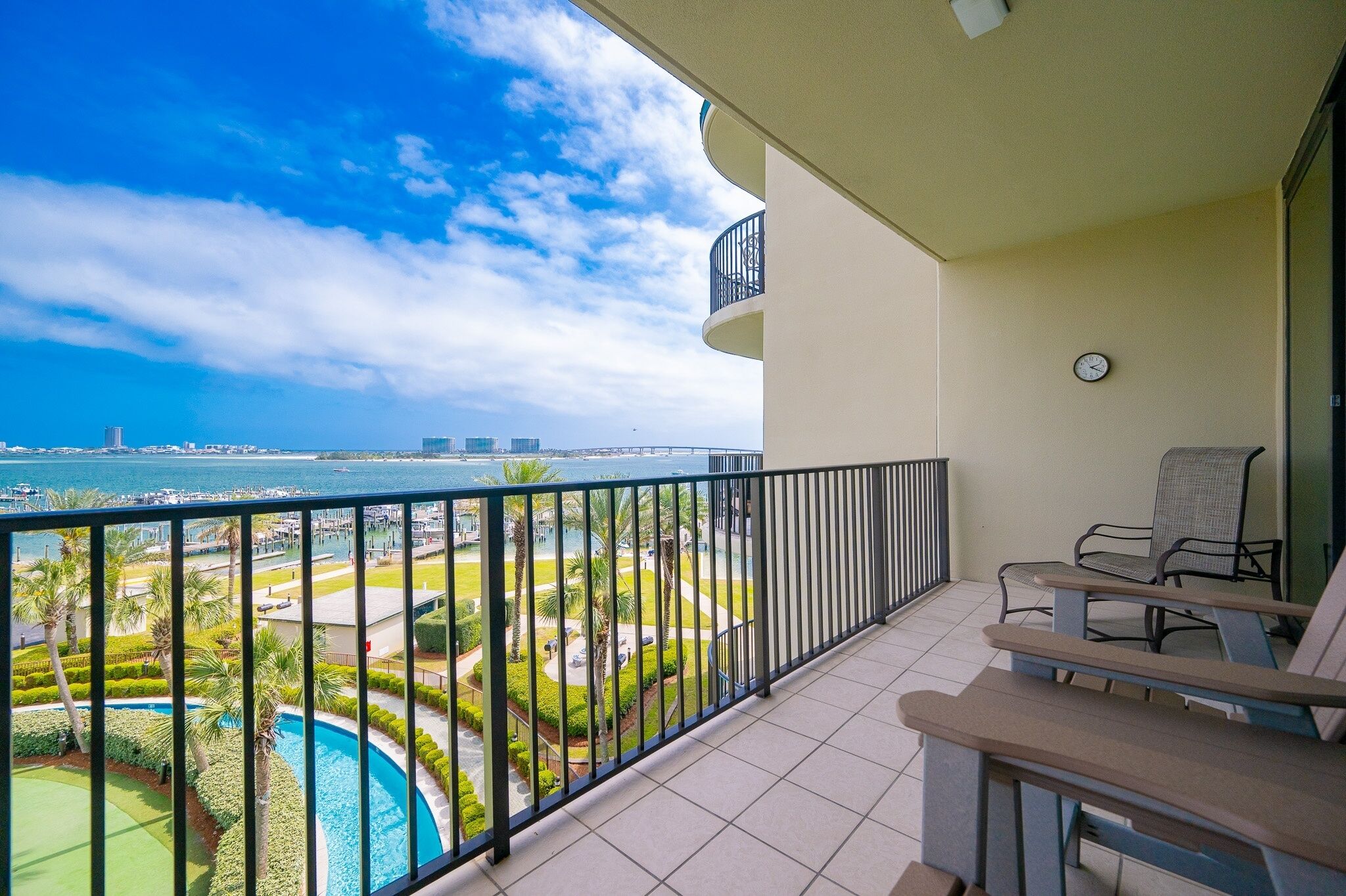 A balcony with a pool view, outdoor seating, and a clock on the wall.