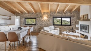 Un intérieur rustique avec des murs en pierre apparentes, des poutres en bois, une cheminée en pierre, un coin repas avec une table et des chaises, et un canapé.