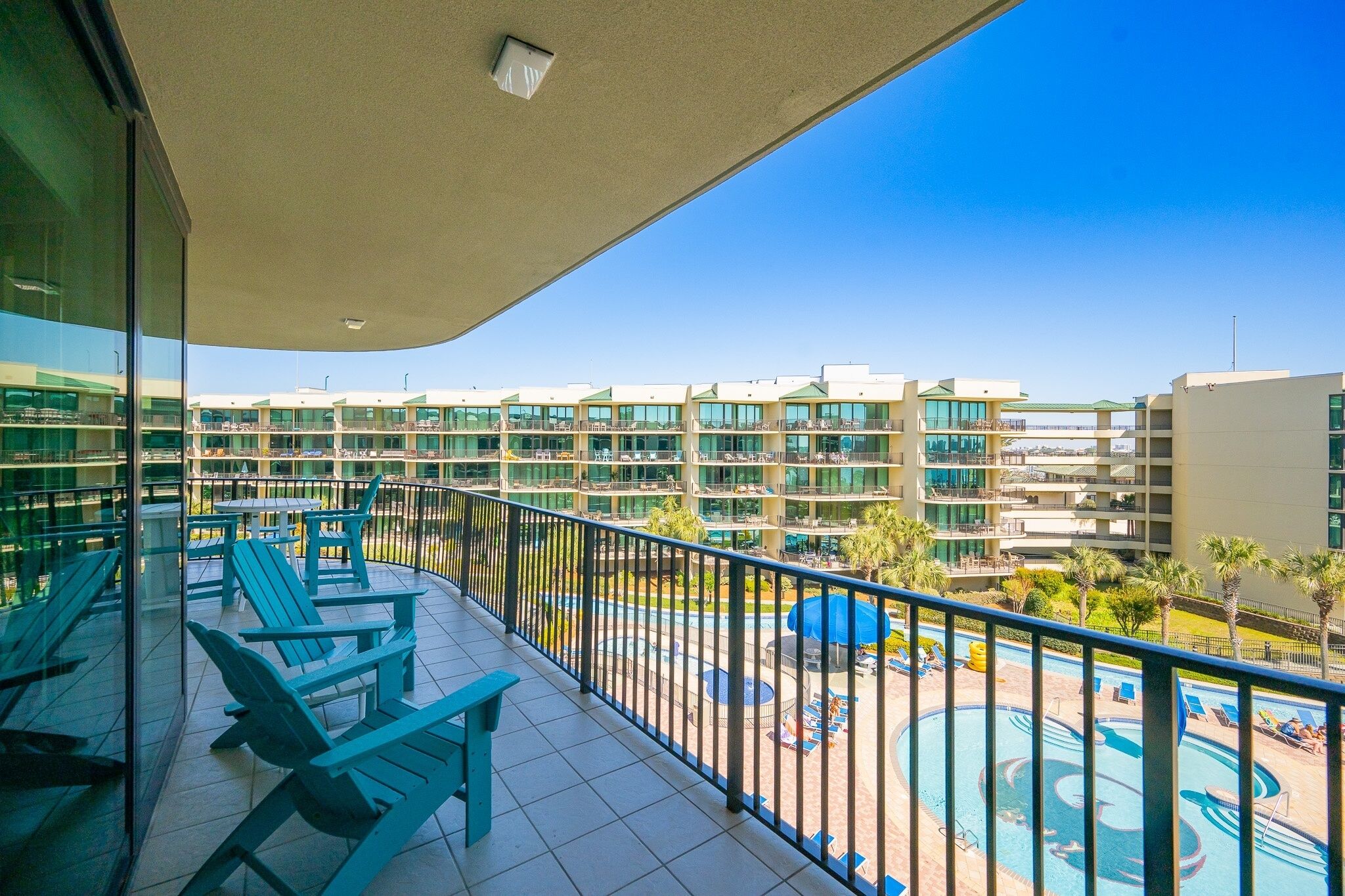 Ein Balkon mit Sitzgelegenheit und Blick auf einen Swimmingpool sowie Hotelgebäude.