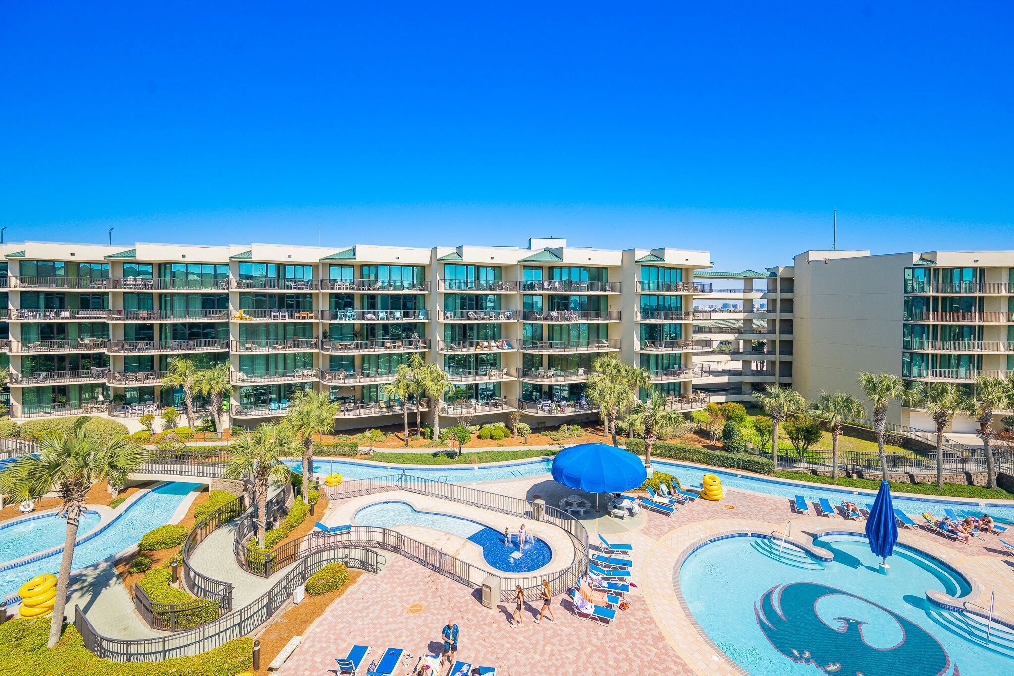 Un hotel con varios balcones, un área de piscina con tumbonas y palmeras.