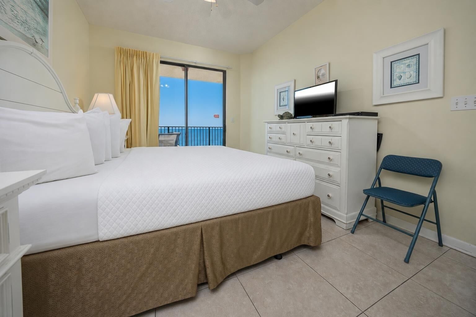 A hotel room with a bed, a dresser, a chair, a TV, and a balcony with a view.