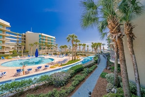 A hotel with a pool, palm trees, and a clear blue sky. - Phoenix On The Bay 1109 3 Bedroom Condo (Orange Beach)