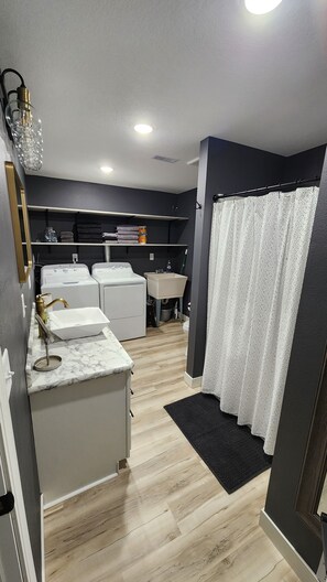 Casa de banho compacta com lavatório, duas máquinas de lavar roupa, espelho e cortina de chuveiro.