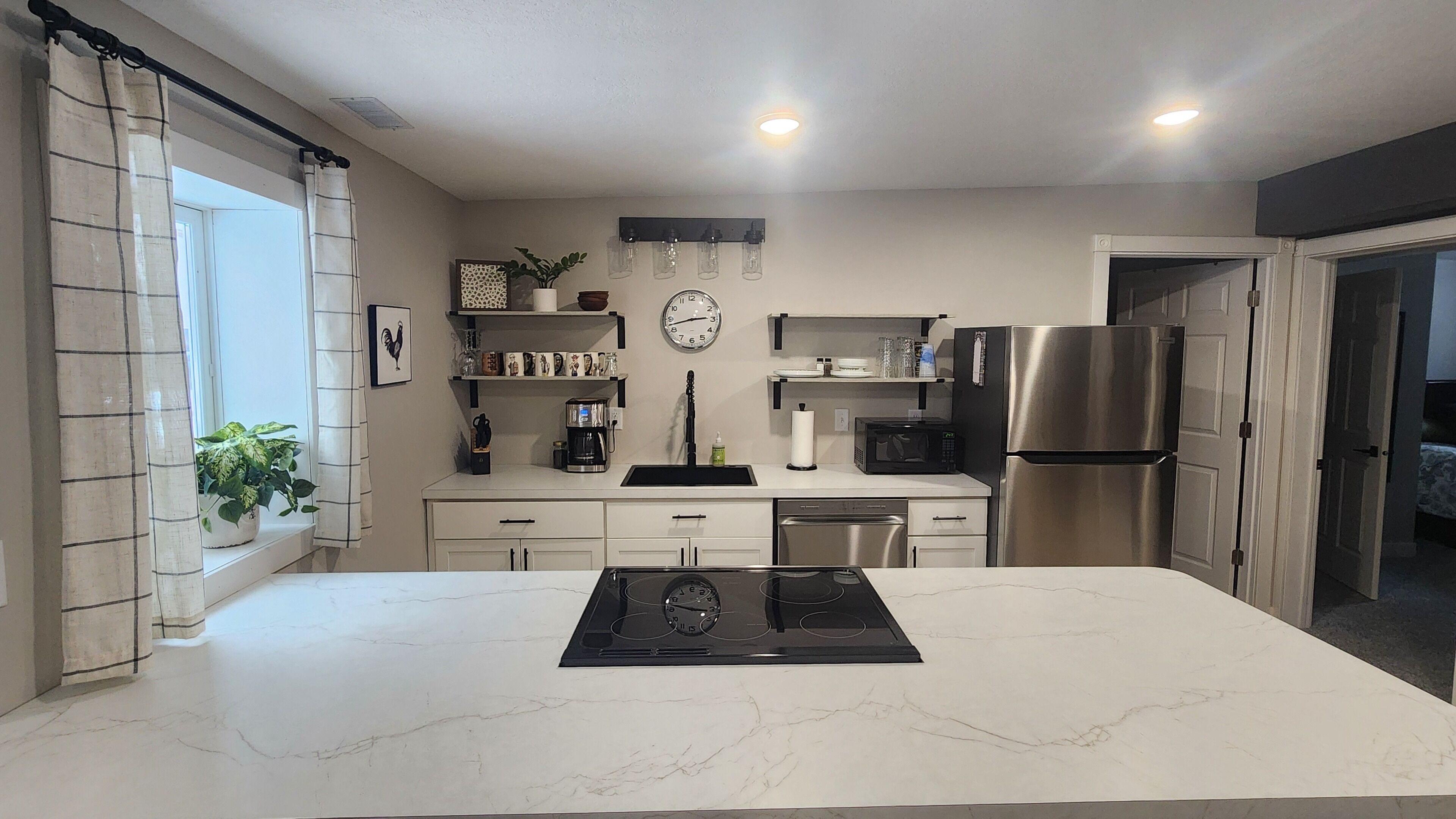 Uma cozinha moderna com uma ilha central, armários brancos, uma geladeira de aço inoxidável e um relógio na parede.