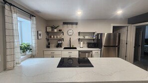 Uma cozinha moderna com uma ilha central, armários brancos, uma geladeira de aço inoxidável e um relógio na parede.