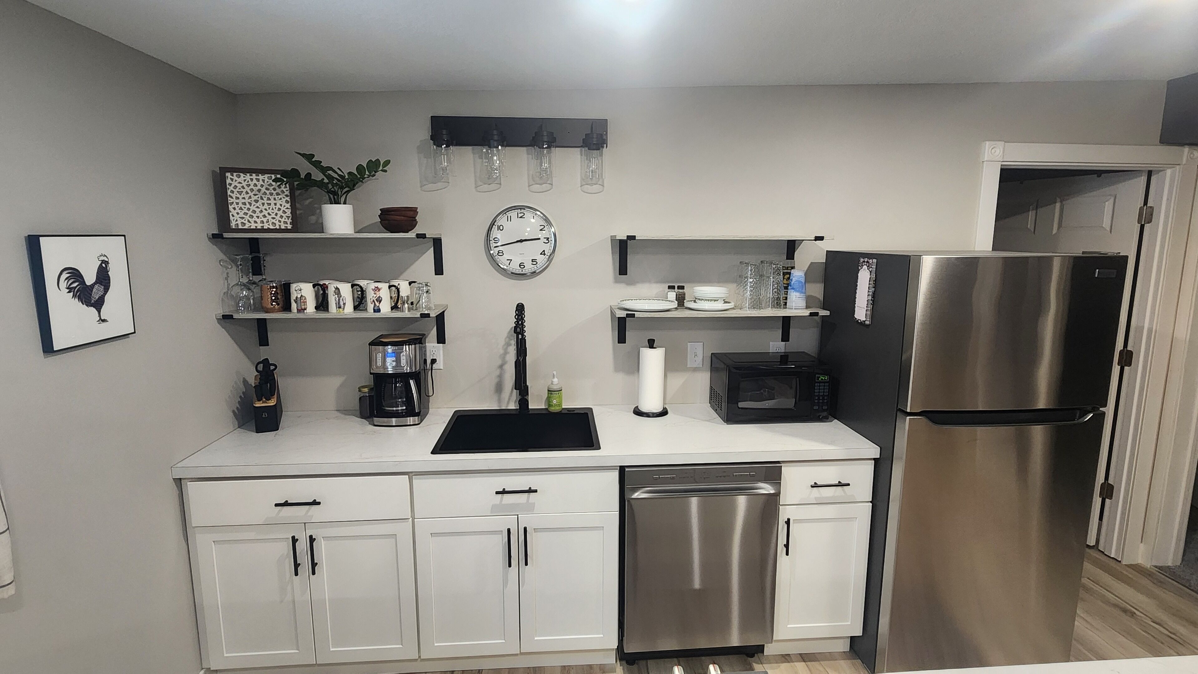 Una cocina moderna con armarios blancos, un refrigerador de acero inoxidable, una cafetera, un microondas y un lavabo.