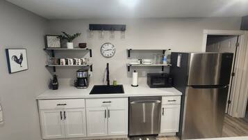Una cocina moderna con armarios blancos, un refrigerador de acero inoxidable, una cafetera, un microondas y un lavabo.