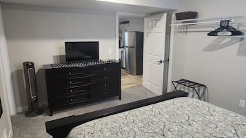 Une chambre à coucher comprenant un lit, une commode, une télévision et une porte donnant sur la cuisine.