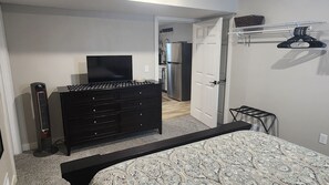 Quarto com cama, cômoda, televisão e porta que dá para uma cozinha.