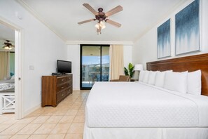 Habitación de hotel con cama, televisión, cómoda de madera, ventilador de techo y balcón con vistas.