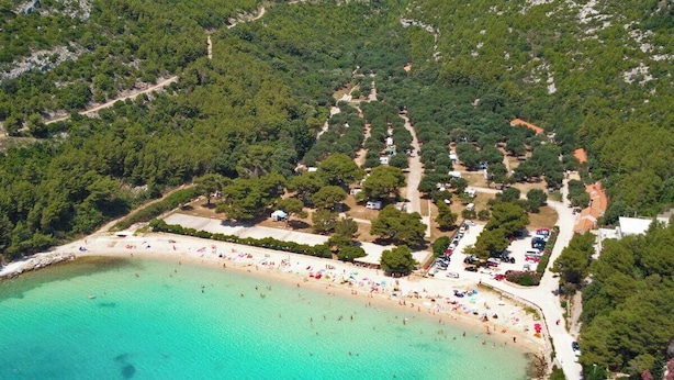 Vue aérienne d’une zone côtière avec une plage, des eaux turquoise et limpides, et une végétation luxuriante.