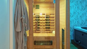 Un sauna aux murs en bois et à la porte en verre, un porte-serviettes et une paire de chaussons posés sur le sol.