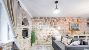 Un salon avec un mur en pierre, un canapé gris, une petite table et une plante en pot.