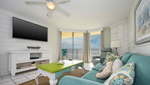 A living room with a flat-screen TV, a green coffee table, a teal sofa, and a balcony with a view. - Phoenix V 509 2 Bedroom Condo (Orange Beach)