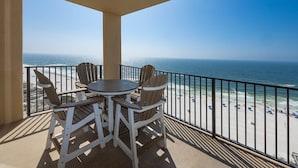 A balcony with a table and chairs, overlooking a beach with people and umbrellas. - Phoenix V 1209 2 Bedroom Condo (Orange Beach)