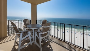 Ein Balkon mit Tisch und Stühlen, der Blick auf einen Strand mit Menschen und Sonnenschirmen bietet.