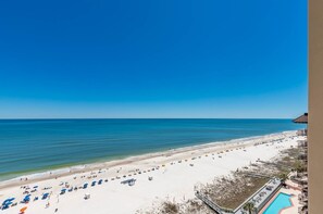 A beach view with a clear sky, a sandy beach, and a pool area. - Phoenix V 1204 2 Bedroom Condo (Orange Beach)