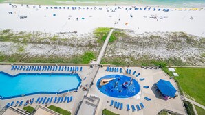 Vista aérea de un complejo turístico en la playa, con piscina, tumbonas y sombrillas.