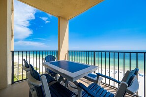 Ein Balkon mit Tisch und Stühlen mit Blick auf einen Strand und einen klaren Himmel.
