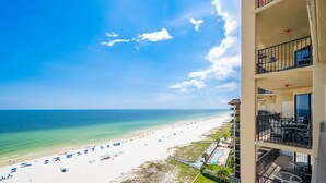 Un hotel frente a la playa con balcones que dan al océano, una piscina y una playa con sombrillas.