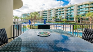 A glass-top table with a decorative plate, a balcony with a view of a hotel building and a pool. - Phoenix On The Bay 1129 2 Bedroom Condo (Orange Beach)