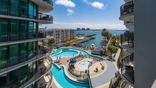 Ein mehrgeschossiges Hotel mit einem zentralen Pool, Sitzgelegenheiten im Freien und Blick auf eine Marina.