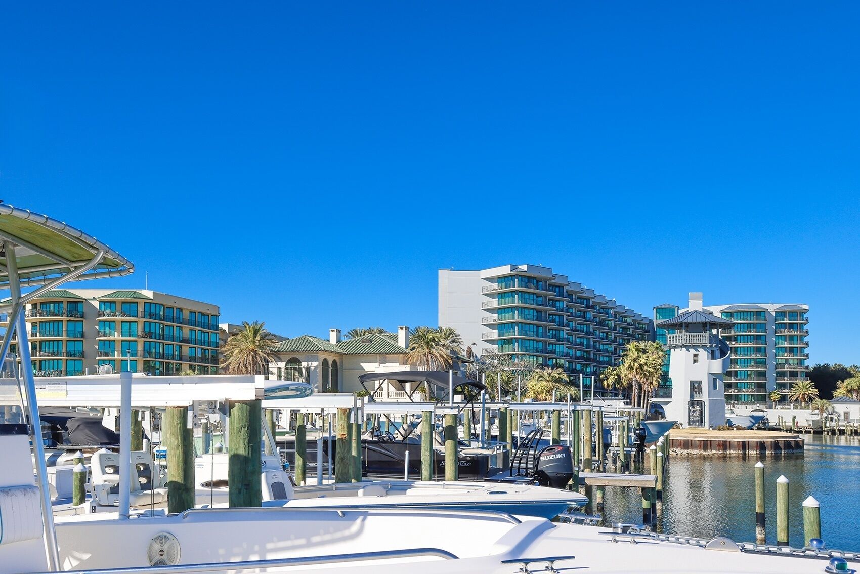 A marina with boats docked, a clear blue sky, and modern buildings in the background.