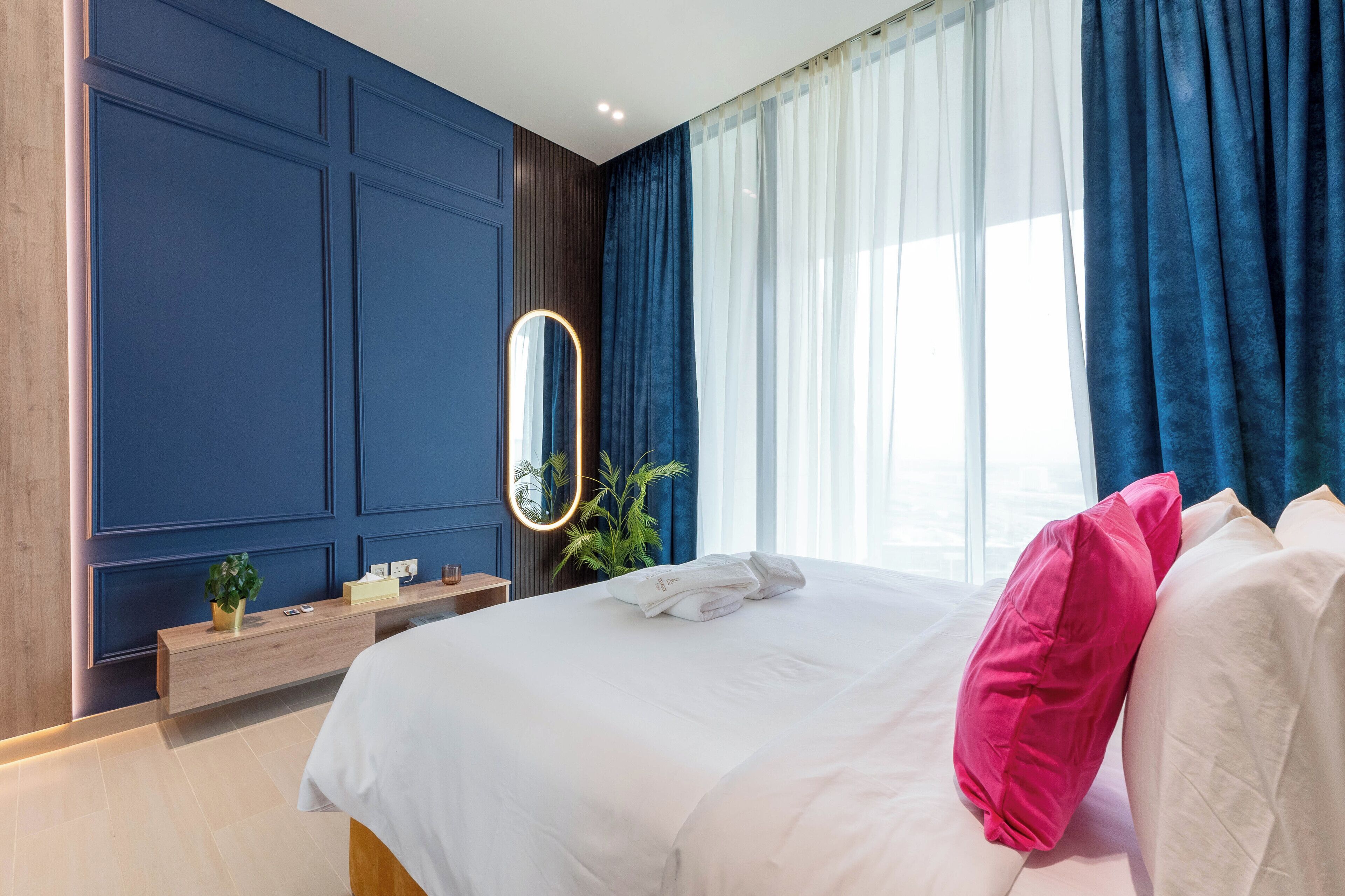 A hotel room with a large bed, a bedside table, a mirror, and a window with curtains.
